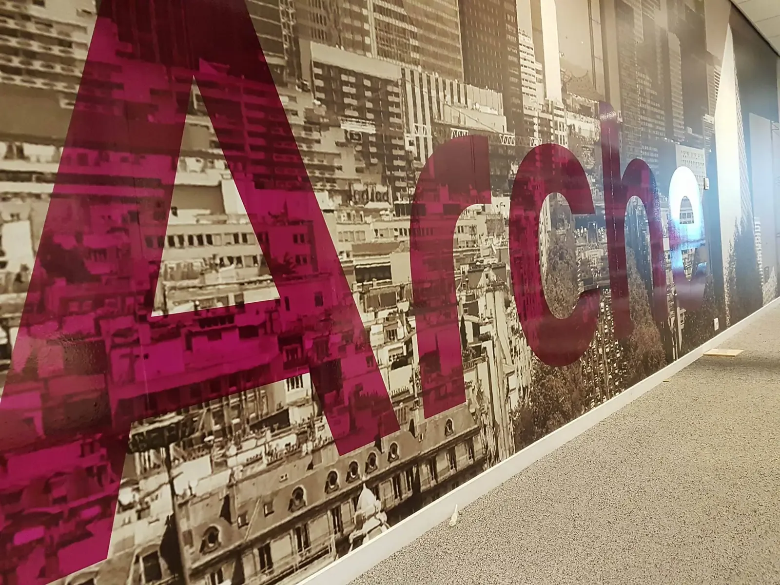 Mot Archi en lettres magenta translucides devant une fresque de ville