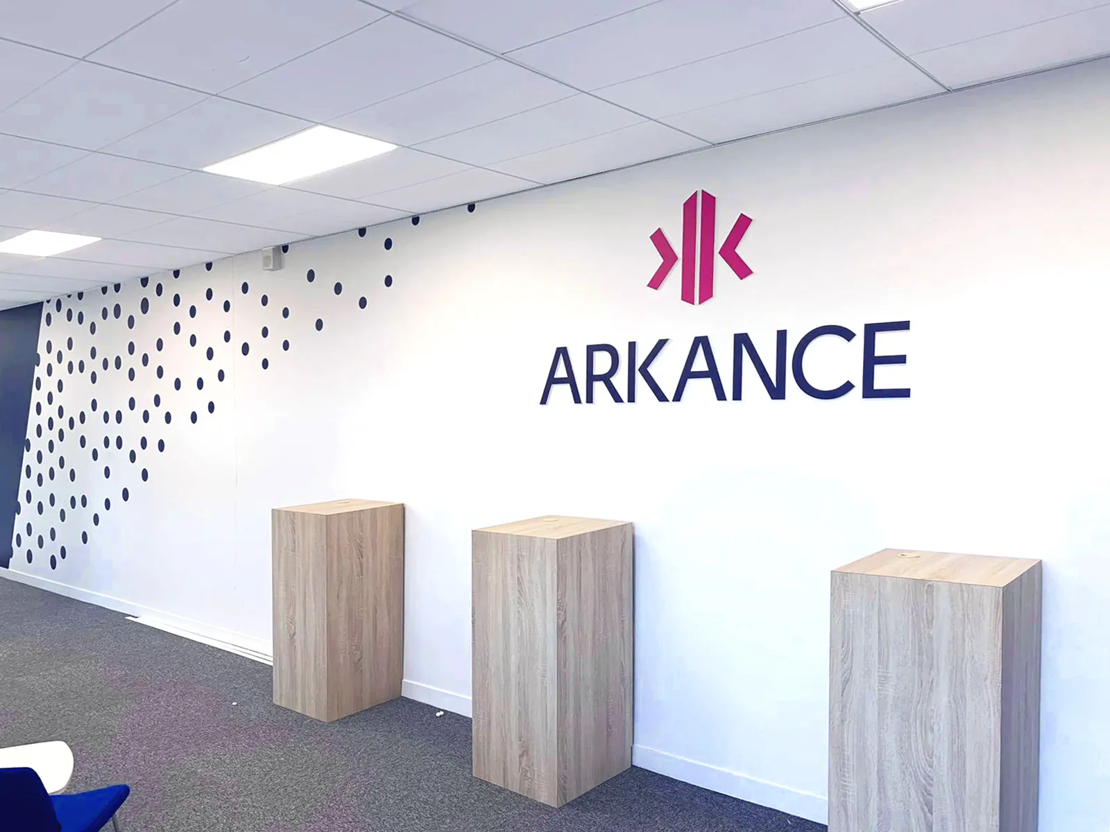 Logo Arkance au-dessus de trois présentoirs en bois dans un hall d'accueil