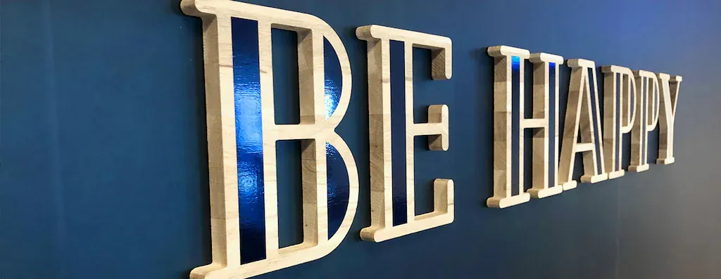 Lettres BE HAPPY en bois clair en relief sur un mur bleu nuit
