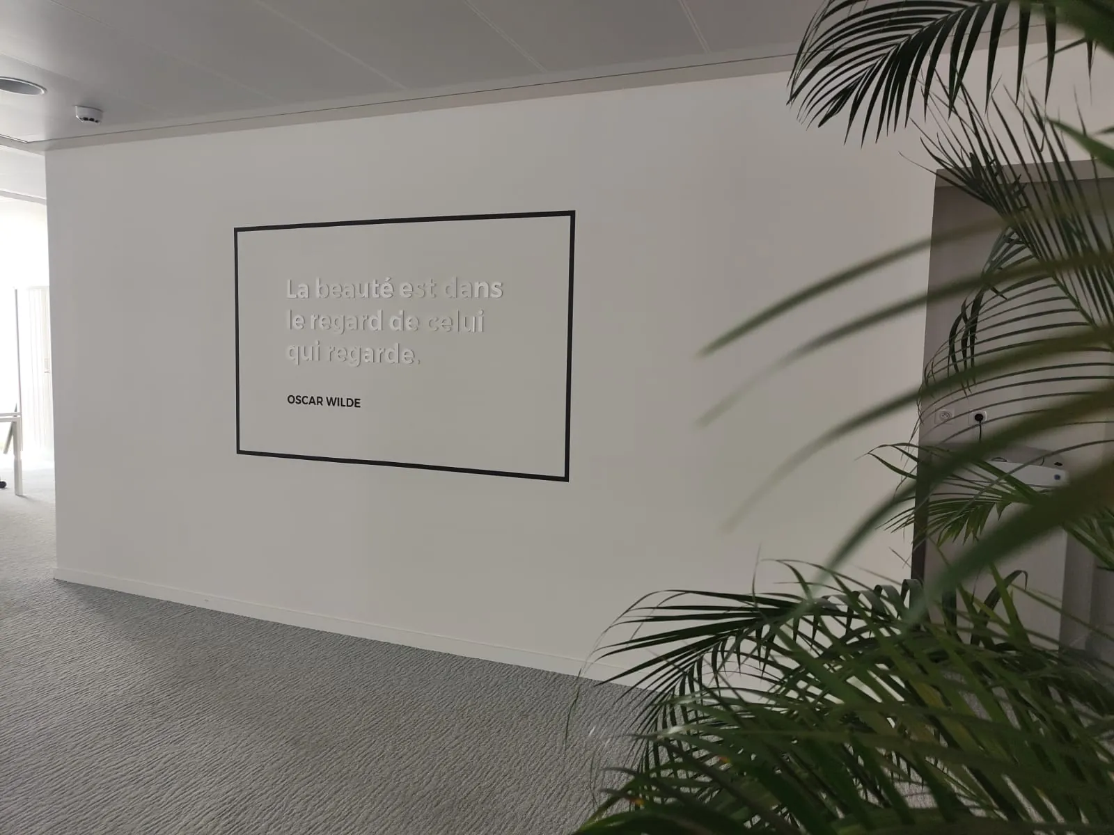 Citation d'Oscar Wilde en lettres blanches dans un cadre noir sur un mur blanc d'open space