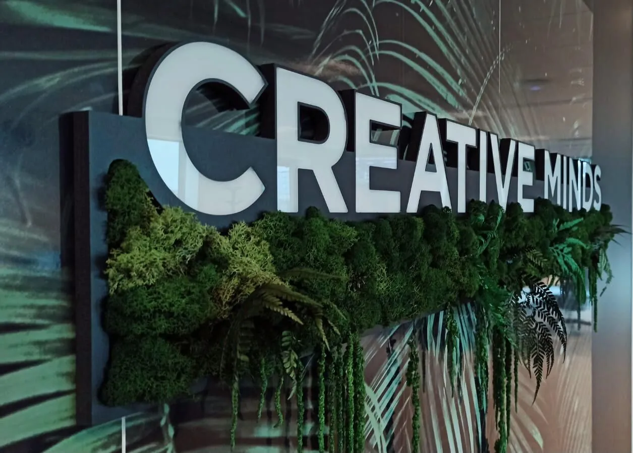 Mots CREATIVE MINDS en lettres blanches en relief au-dessus d'un bandeau de végétal stabilisé