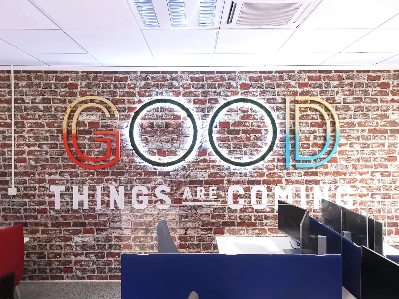 Mot GOOD en grandes lettres lumineuses de couleur et THINGS ARE COMING en lettres blanches sur un mur de briques