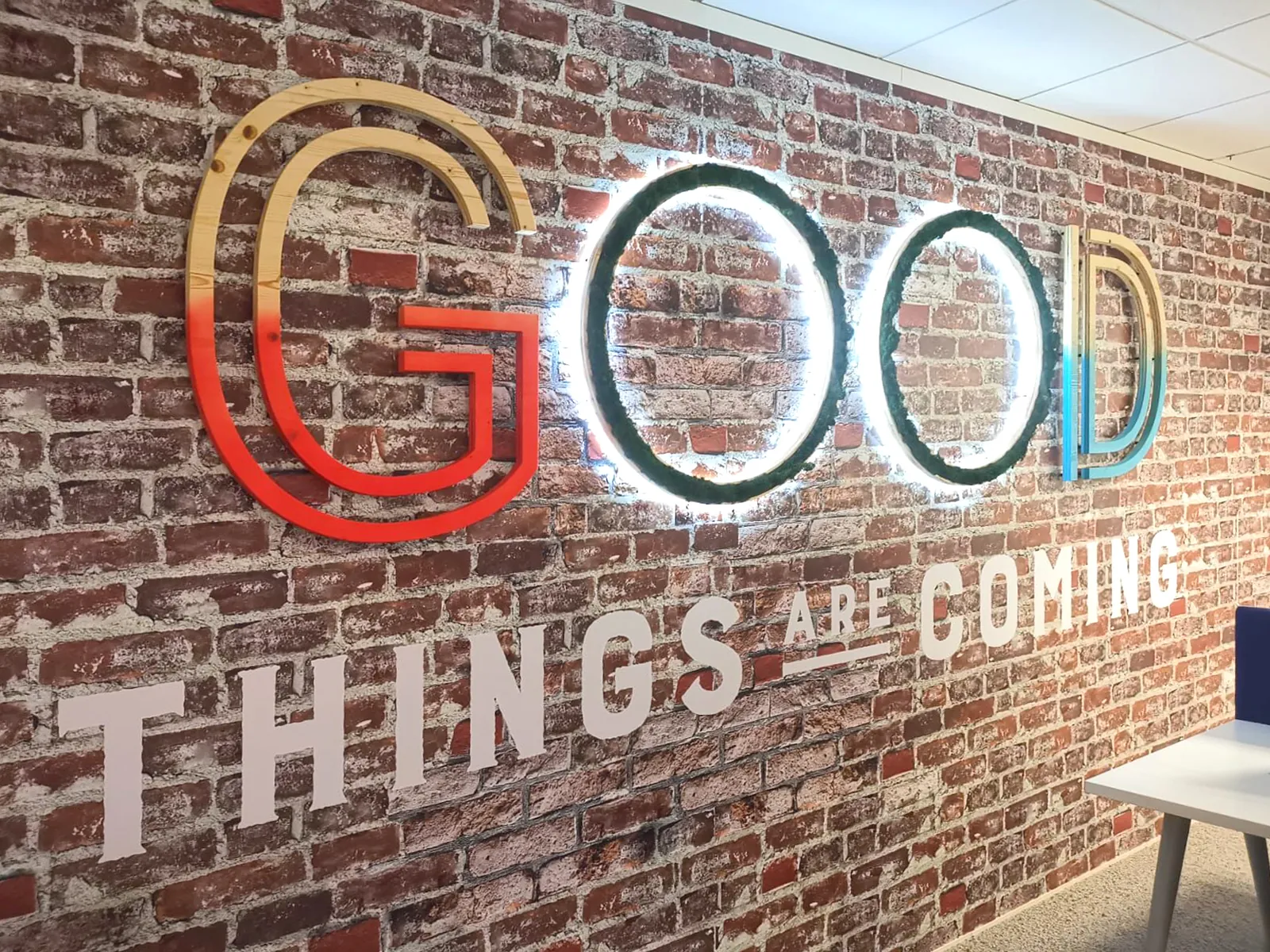 Lettres GOOD rétroéclairées en couleur, vues de biais sur un mur de briques
