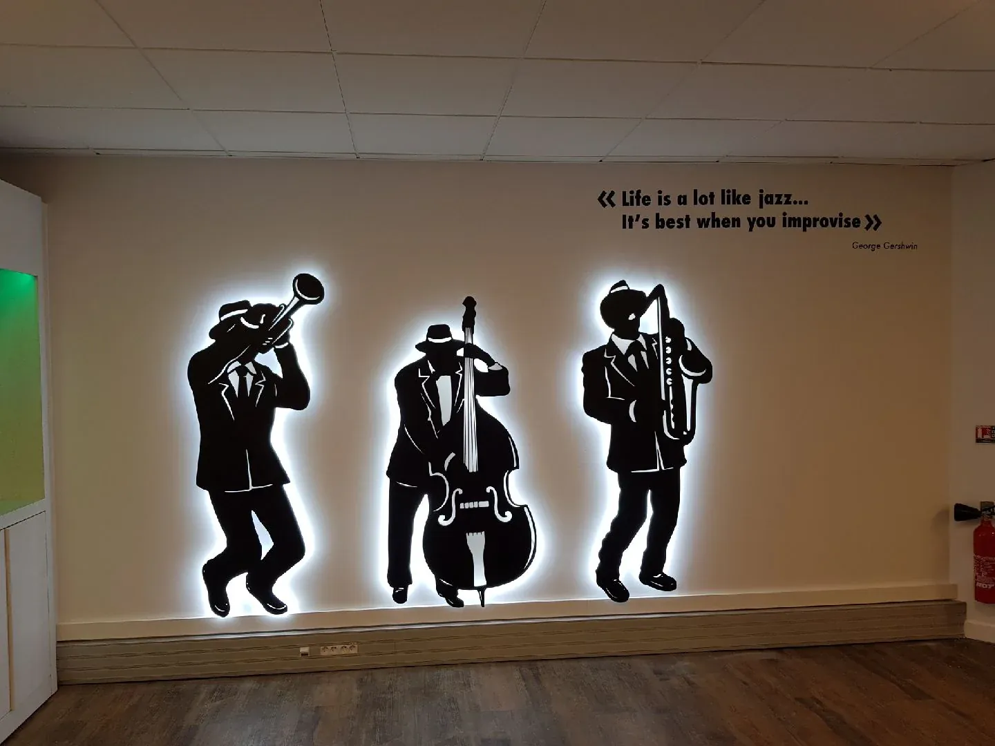 Silhouettes noires de trois musiciens de jazz rétroéclairées sur un mur blanc, sous la citation « Life is a lot like jazz »