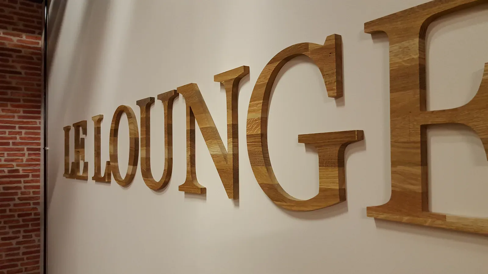 Mot LE LOUNGE en grandes lettres de bois sur un mur blanc