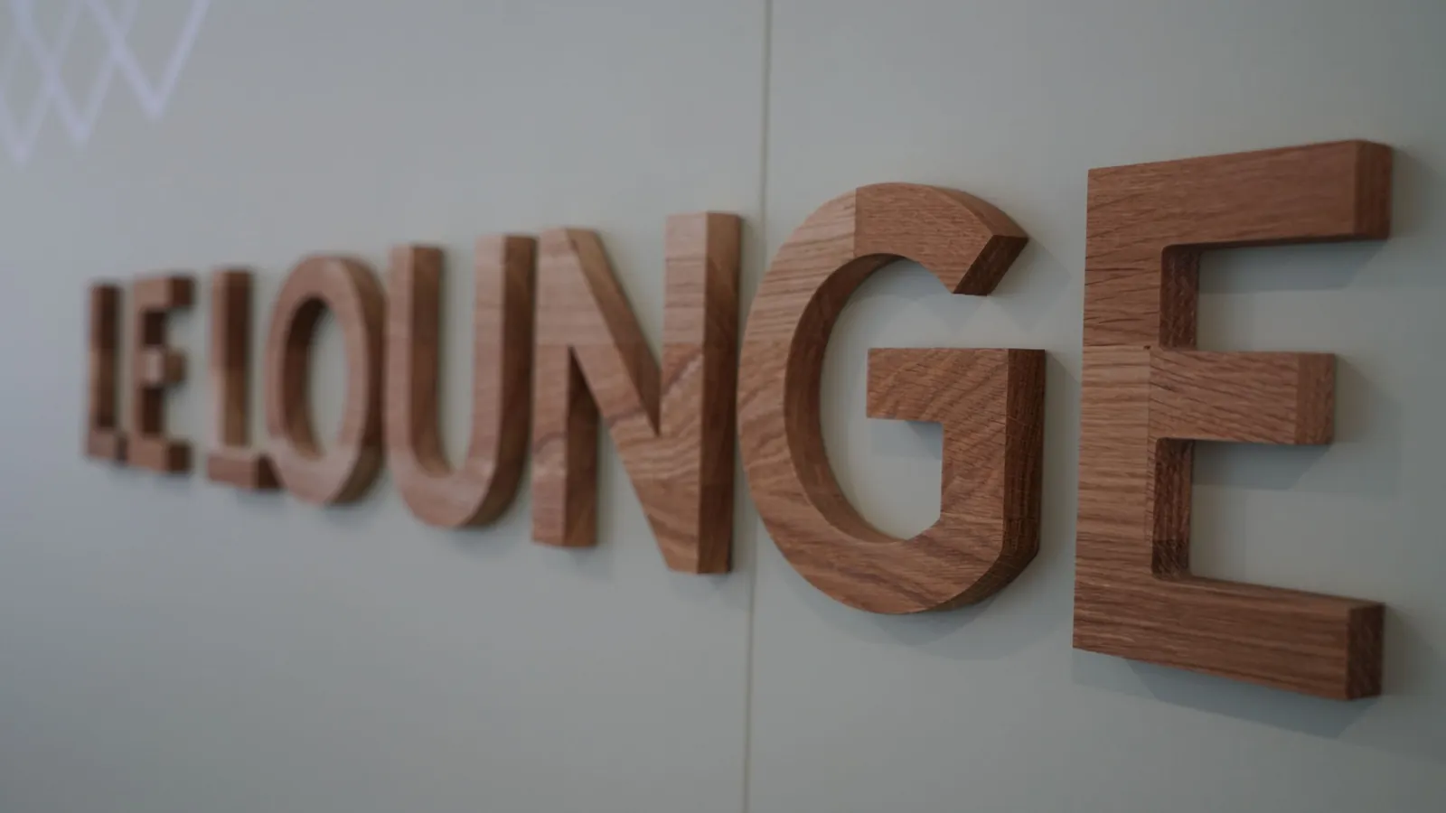 Mot LE LOUNGE en lettres de bois épaisses, vues de biais sur un mur gris