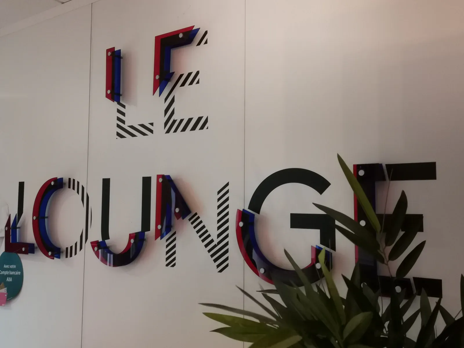 Mot LE LOUNGE en lettres superposées rouge, bleu et noir, fixées à distance du mur