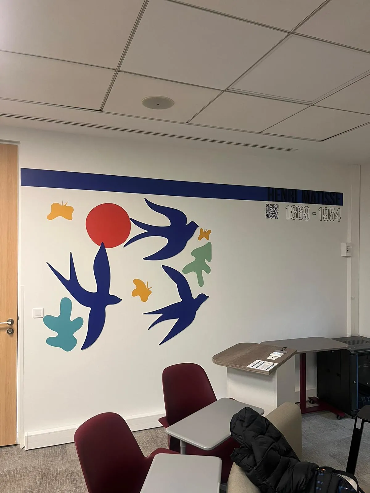Hirondelles, soleil et feuilles découpés en couleur sur le mur blanc d'une salle de pause