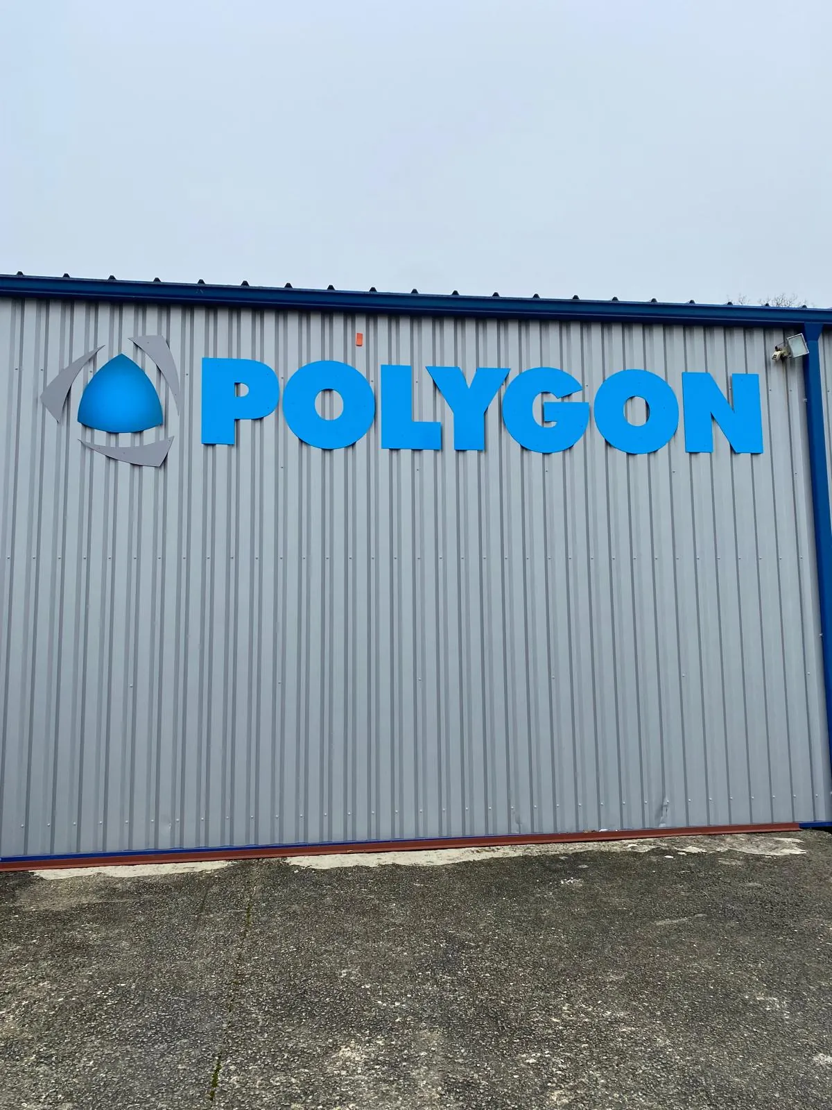 Logo Polygon en lettres bleues en relief sur la façade en bardage d'un bâtiment industriel