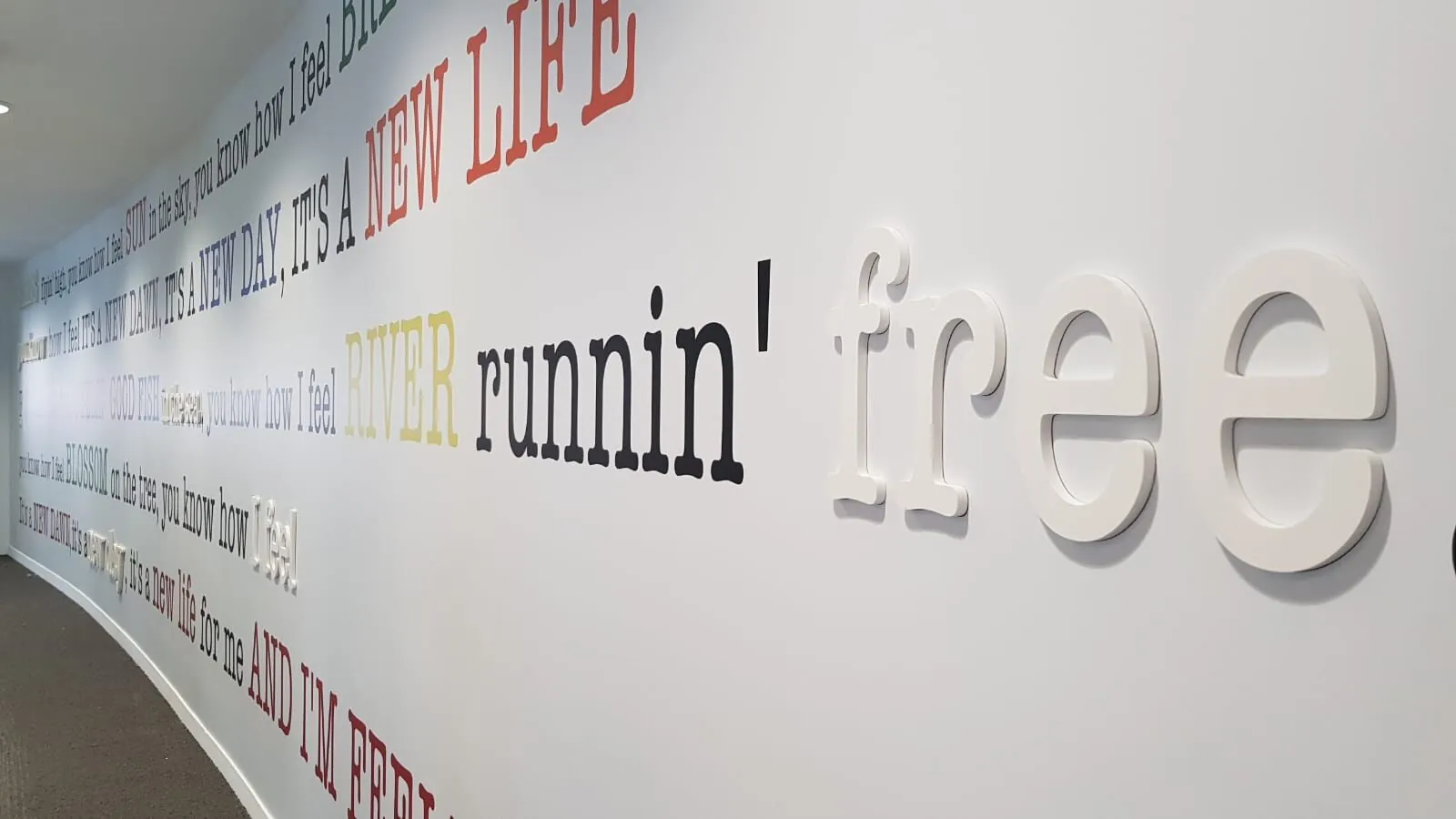 Paroles de chanson en lettres PVC blanches et de couleur le long d'un mur, vue en perspective