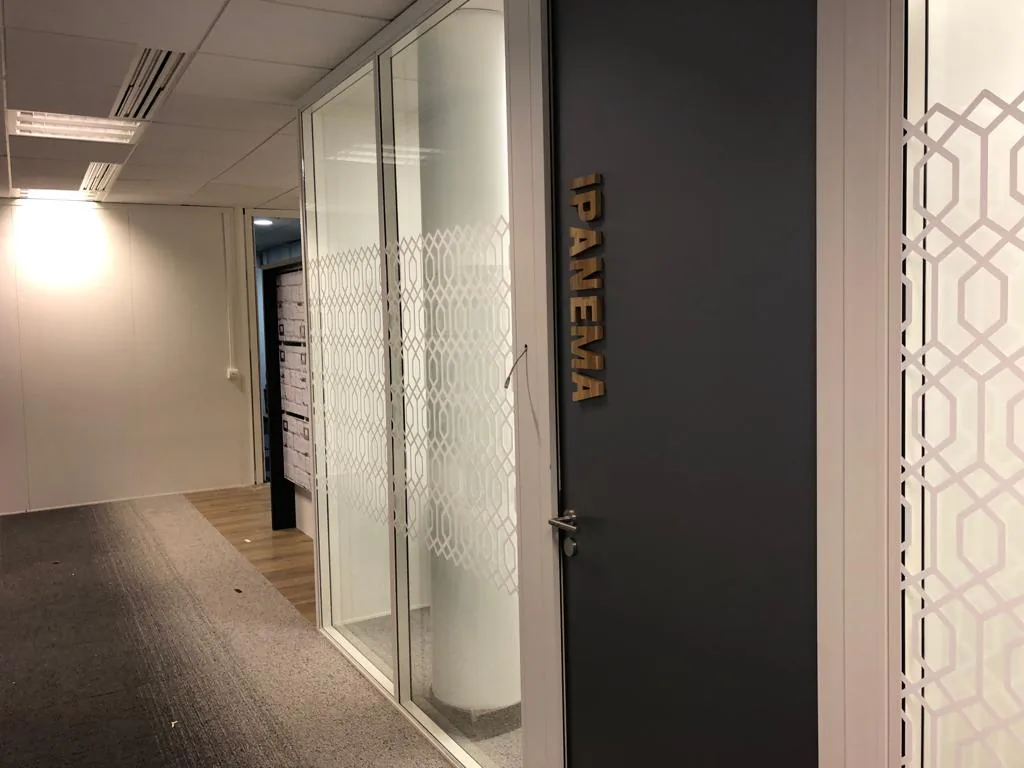 Nom de salle Ipanema en petites lettres bois sur porte, devant cloison vitrée dépolie