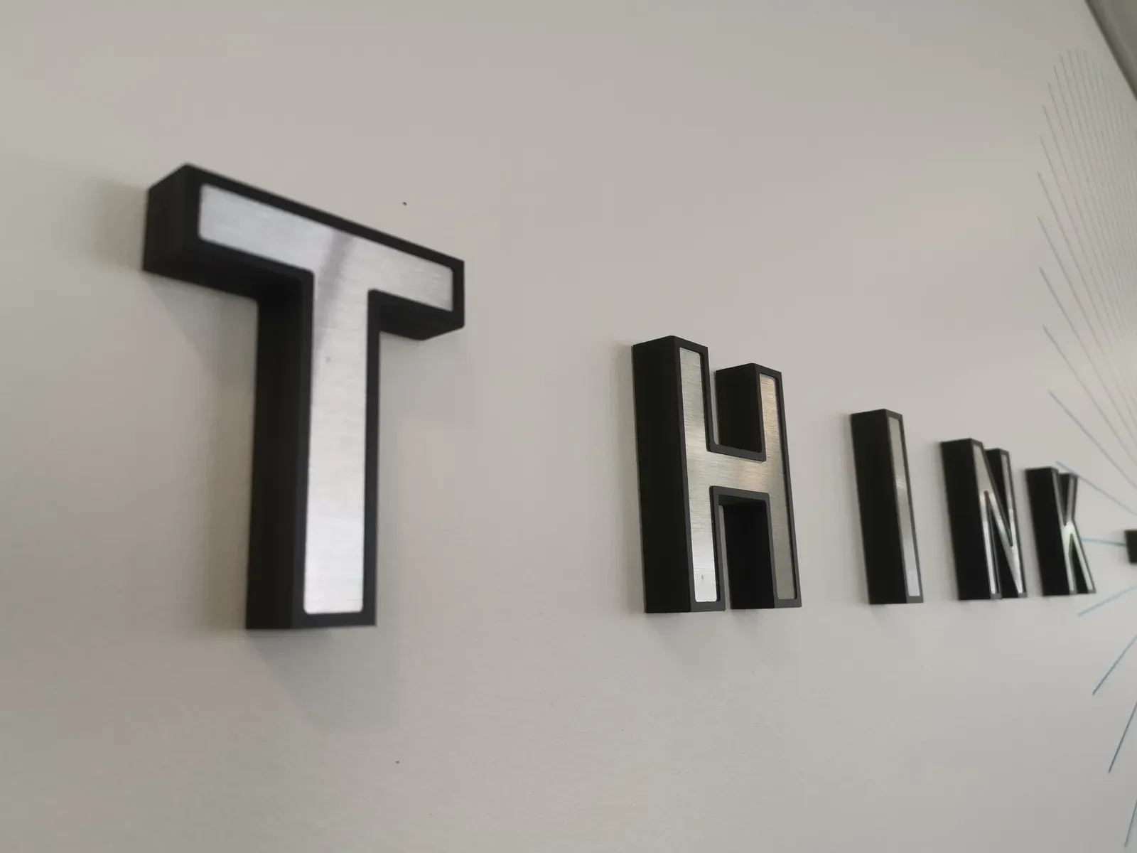 Lettres THINK en relief, faces claires et chants noirs, sur un mur blanc