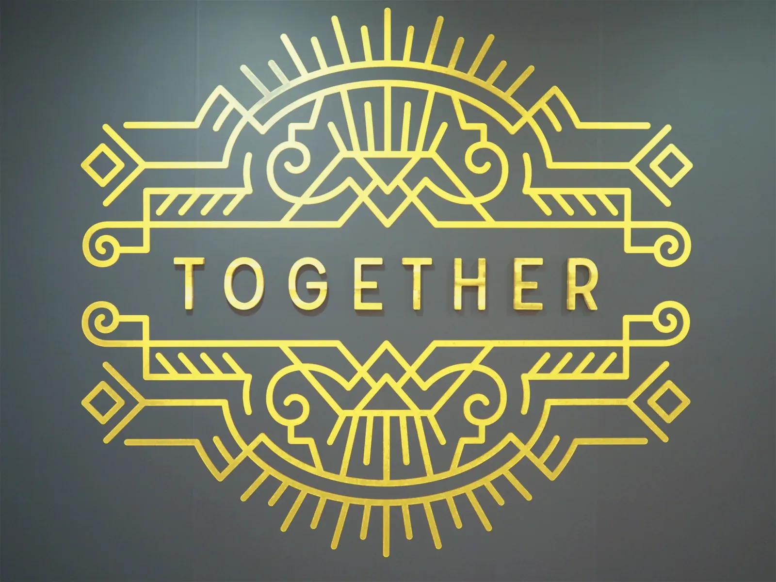 Logo Together doré découpé, motif Art déco, sur un mur bleu nuit