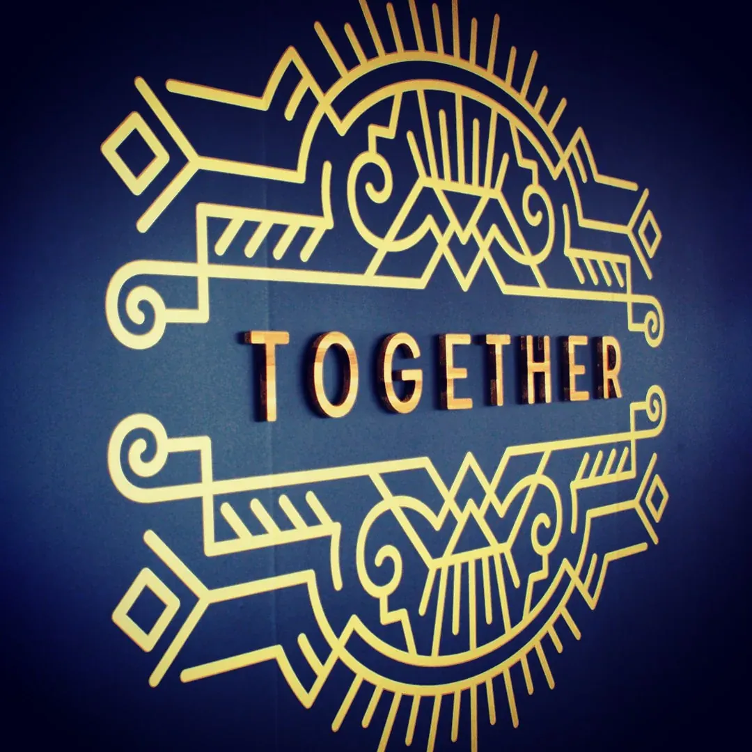 Emblème Together doré en relief, vu de biais sur un mur bleu nuit