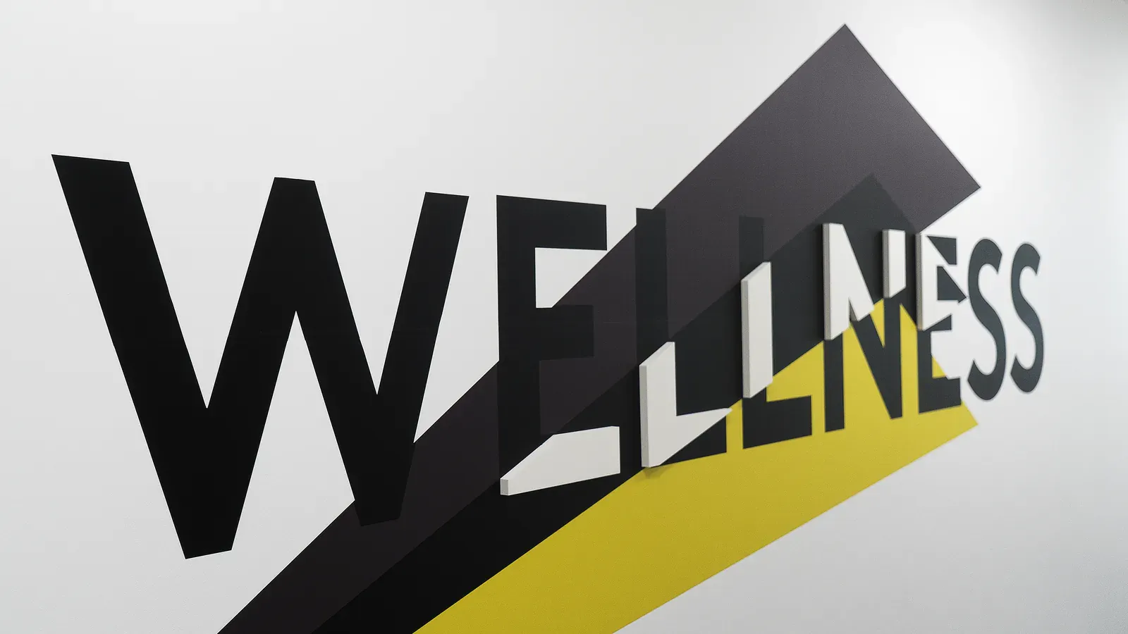 Mot WELLNESS en grandes lettres noires en relief traversé d'une bande jaune